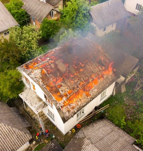 Aerial view of a house on fire with orange flames and white thick smoke.