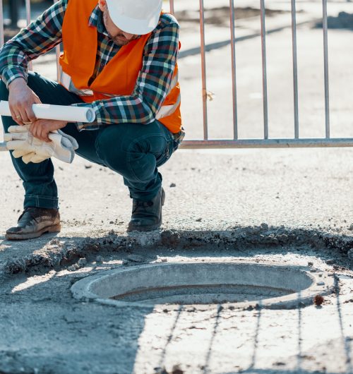 Engineer in reflective vest standing near a hole in the road during carriageway work