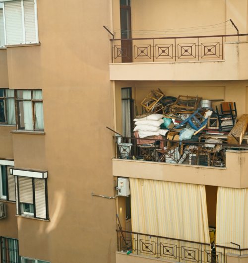 Ugly, terrible balcony disorder. Multi-storey building full of garbage, old furniture, unnecessary things, boxes,chairs, pillows, clothes, window frames. Incorrect storage organization, balcony trash.